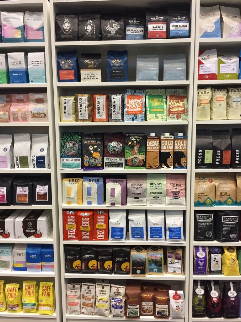Shelves displaying coffee bags from many specialty coffee roasters at a coffee show.