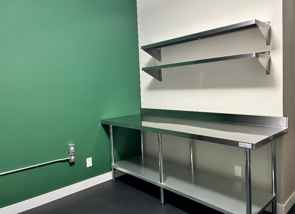 Stainless-steel worktable and wall shelves installed beside the green wall in the Filgap Coffee roasting room.