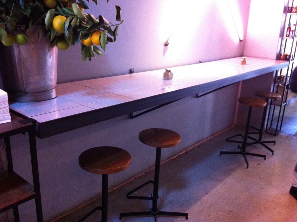 Long tiled counter with timber stools and dark steel frames inside Reuben Hills.
