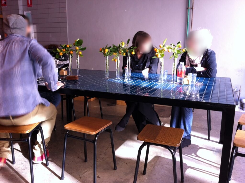 Large dark tiled communal table surrounded by timber stools inside Reuben Hills.