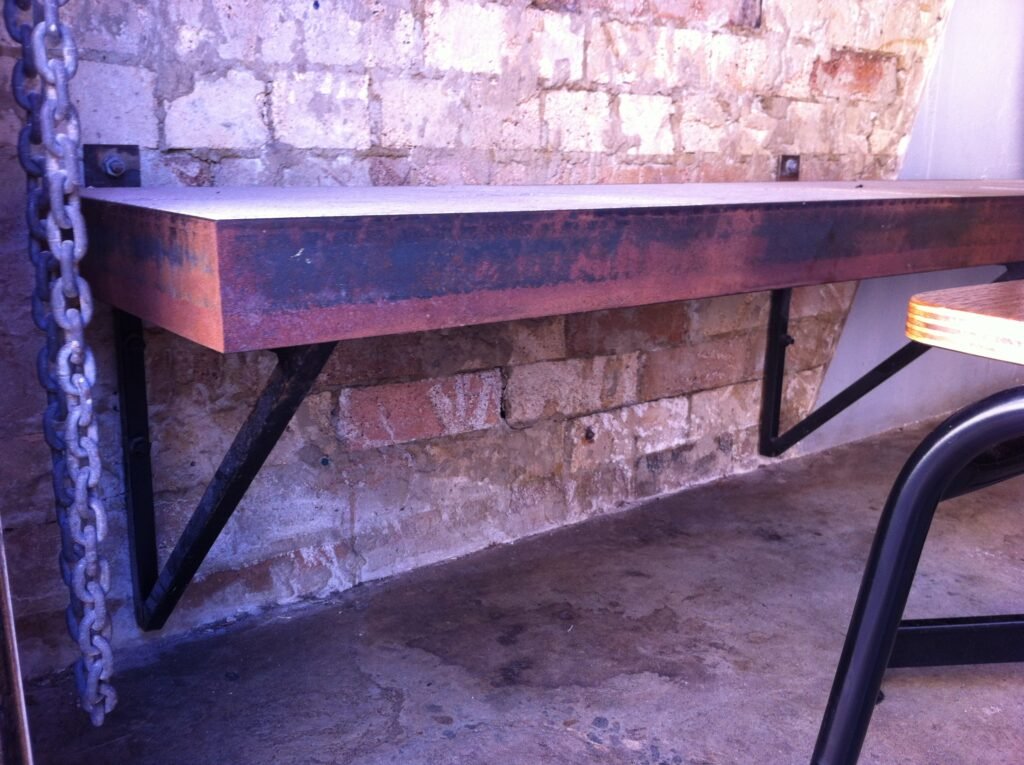 Wall-mounted bench with an exposed steel frame against an old brick wall at Reuben Hills.