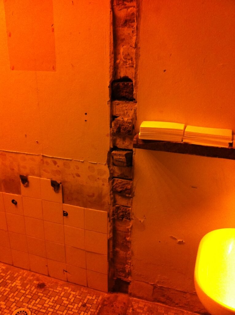 Bathroom wall at Reuben Hills showing old tiles, exposed brick and partially stripped wall surfaces.