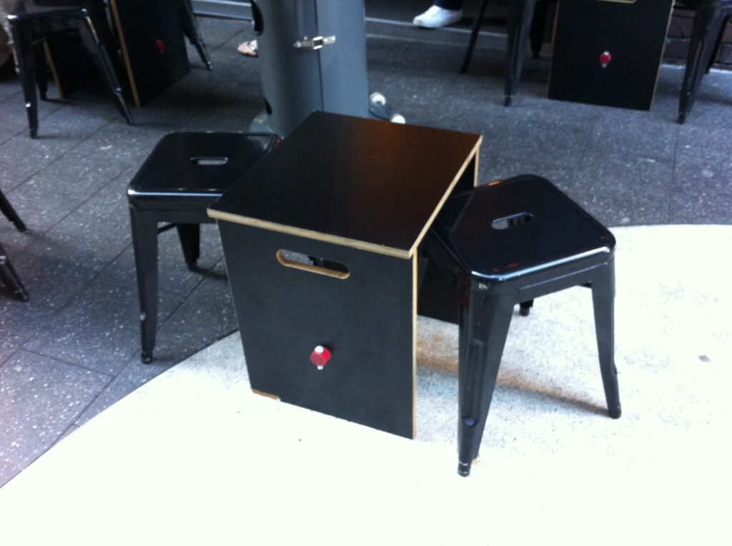 Small black box-style outdoor table between two black metal stools outside Room 10.