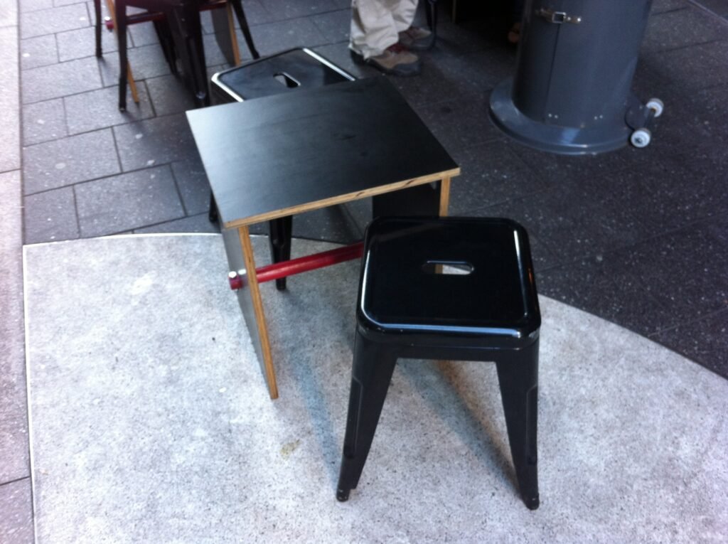 Small low black outdoor table with a black metal stool on the pavement outside Room 10.