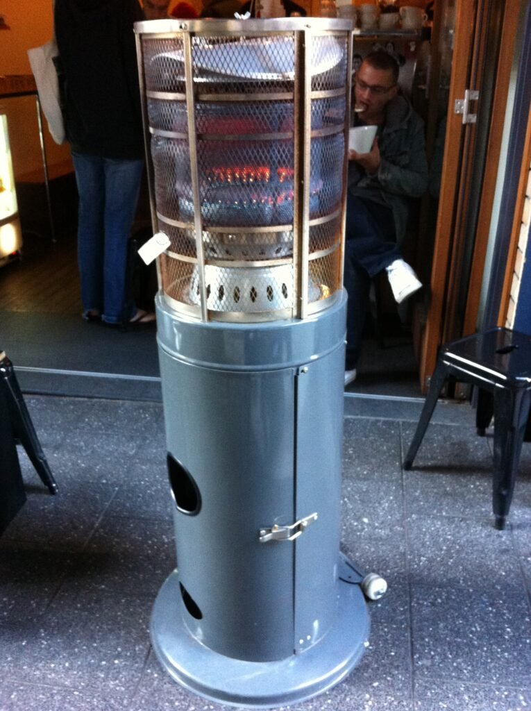 Tall freestanding gas heater positioned among outdoor stools beside the entrance to Room 10.