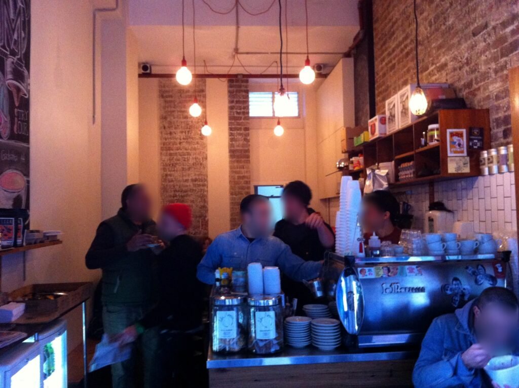 Wide view inside Room 10 showing customers, the espresso bar, food preparation area, open shelving and exposed brick walls.