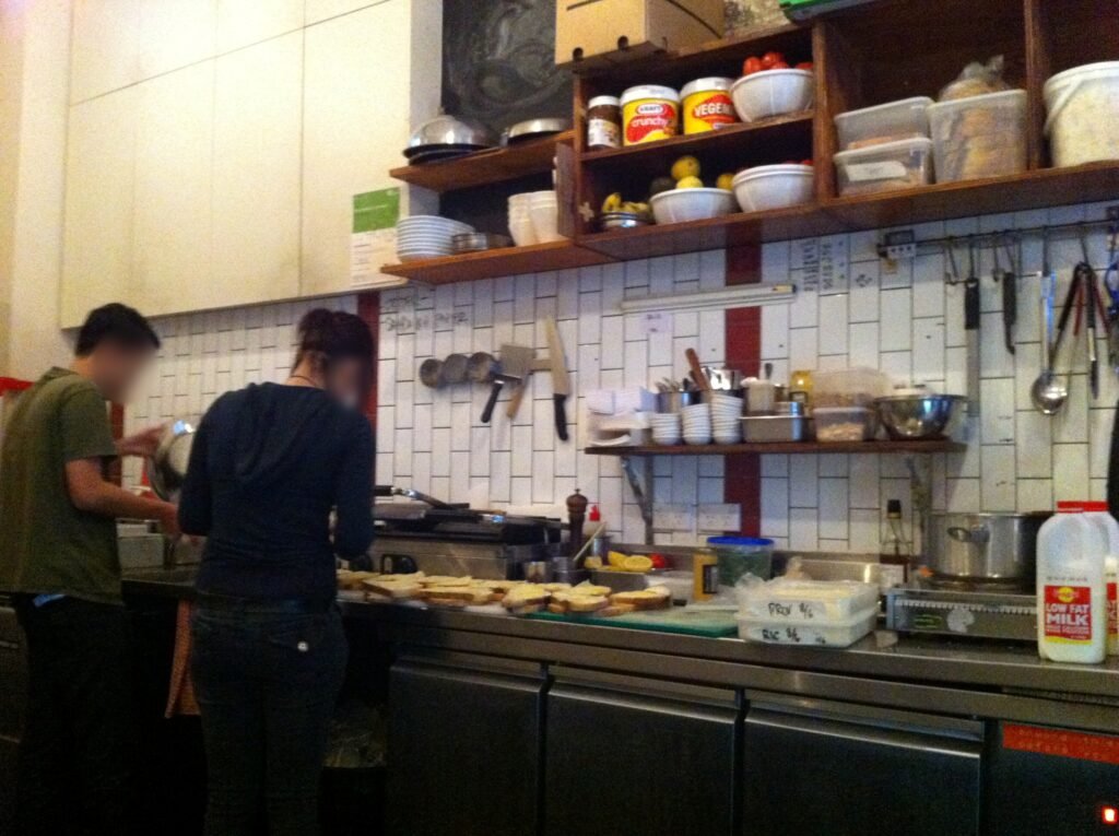 Two staff preparing food along a stainless-steel counter with open shelves and cooking equipment at Room 10.