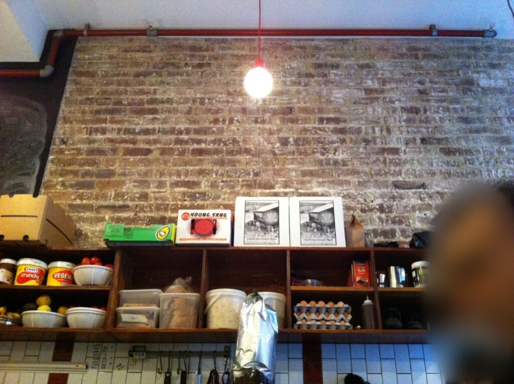 Long open wooden shelves holding bowls, containers, eggs and ingredients above the food-preparation area at Room 10.