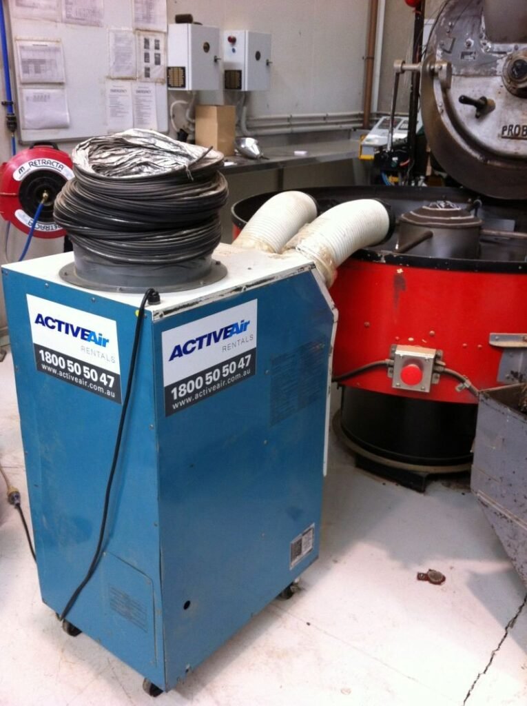 Blue portable air unit with flexible ducts positioned beside a red coffee-roaster cooling tray