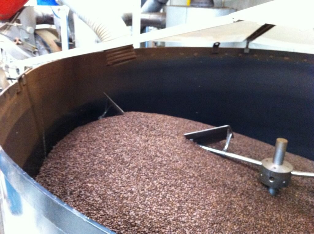 Roasted coffee beans spread across a circular cooling tray with metal stirring arms