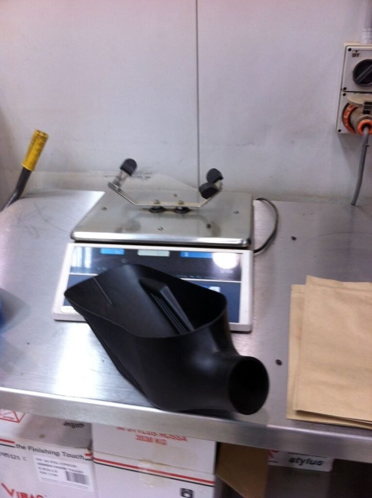 Bench scale with a black coffee sample scoop and brown paper bags on a stainless-steel table